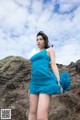 A woman in a blue dress standing on a rocky beach.