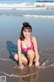 A woman in a pink bikini sitting on the beach.