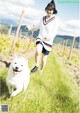 A woman walking a white dog on a leash in a field.