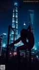 A woman sitting on a railing in front of a city at night.