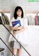 A woman standing in front of a white brick wall holding a book.