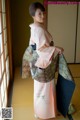 A woman in a pink kimono standing in front of a window.