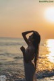 A woman in a white dress standing on the beach at sunset.