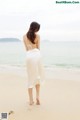 A woman in a white dress walking on the beach.