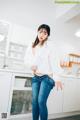 A woman in a white shirt and jeans posing in a kitchen.