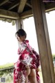 A woman in a red kimono standing under a wooden structure.