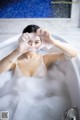 A woman in a bathtub making a heart with her hands.