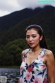 A woman in a floral dress standing by a lake.