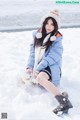 A woman sitting in the snow wearing a blue jacket and hat.