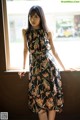 A woman in a floral dress leaning against a window.