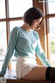 A woman sitting on top of a wooden table next to a window.