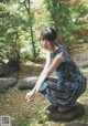 A woman in a blue dress crouching on a rock in a garden.