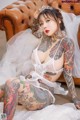 A woman with tattoos sitting on a couch wearing a wedding dress.