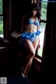 A woman in a blue bikini sitting by a window.